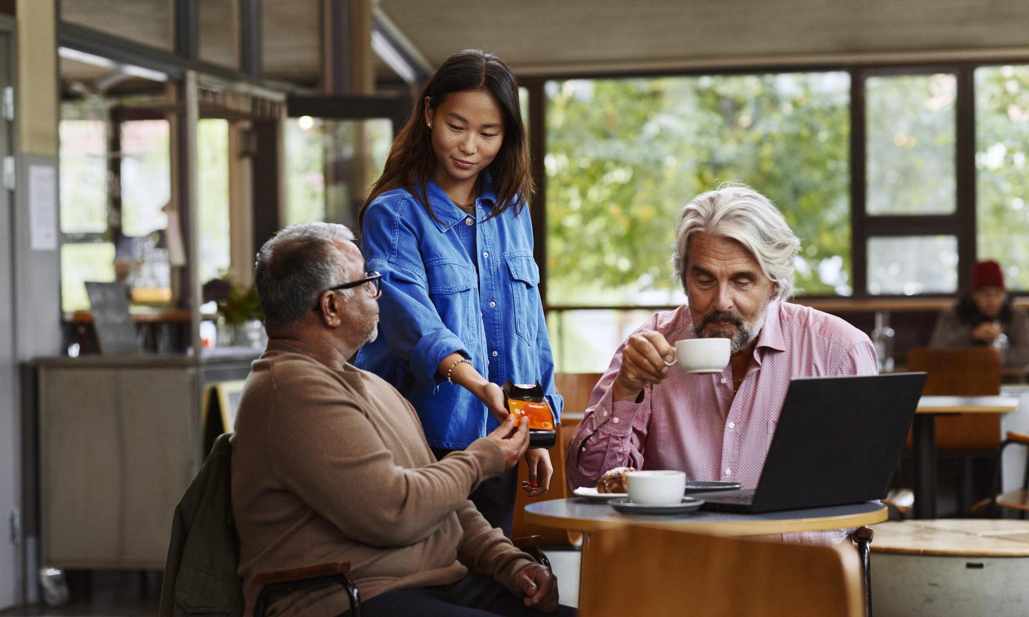 Two men with a laptop paying for their coffee in a café 