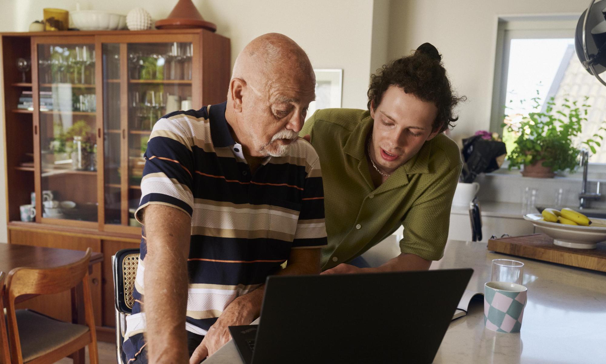 A young man and a senior discussing in front of a laptop