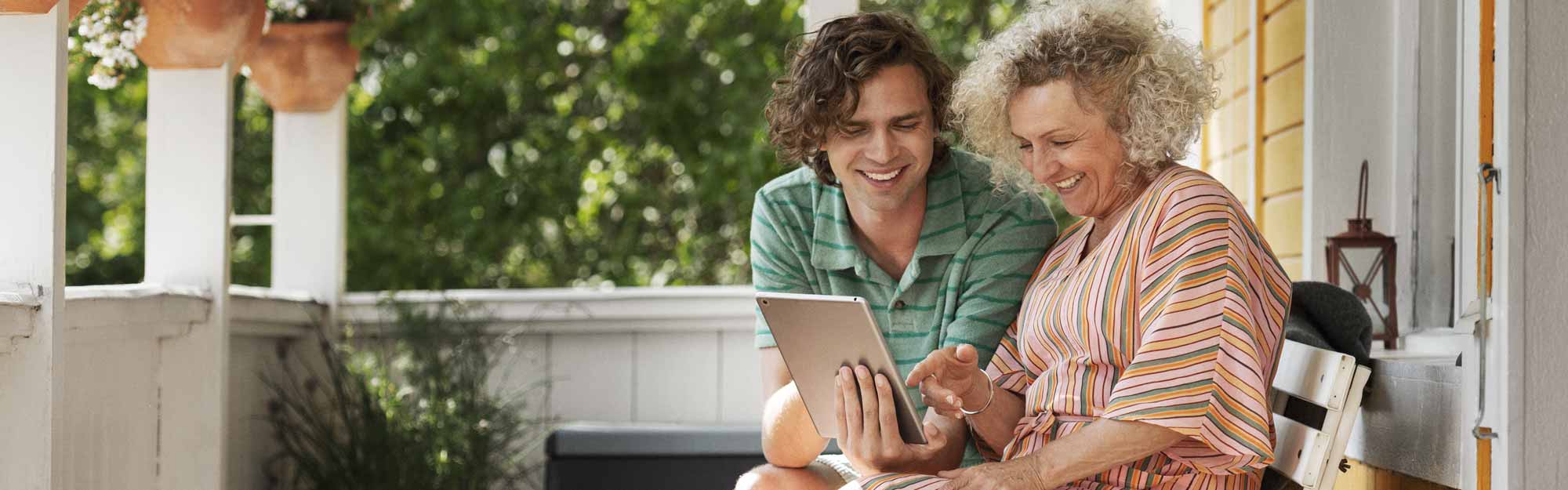 Mamma och vuxen son sitter på verandan och tittar på en surfplatta