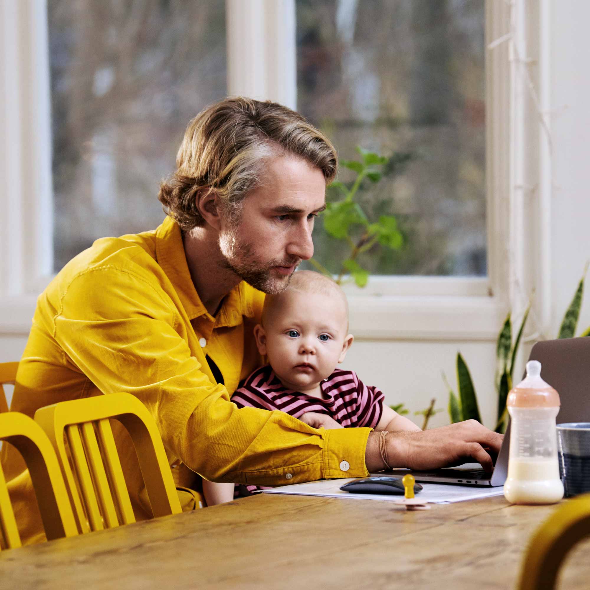 Pappa tittar på datorn med bebisen i knät