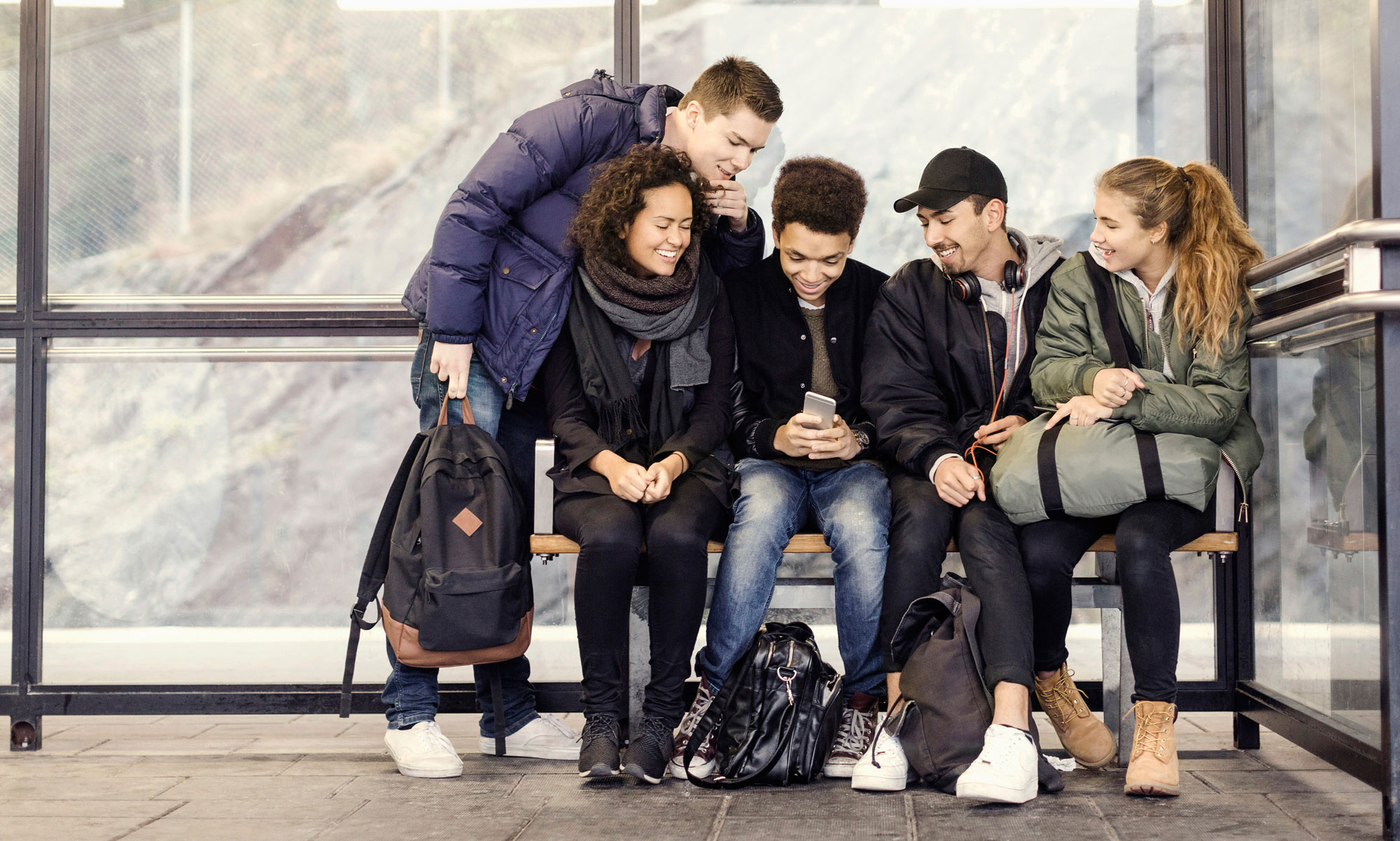 Ungdomar sitter och väntar på bussen och tittar på en mobil